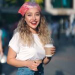 Portrait of women in white blouse, red headband and jean holding a coffee on the street